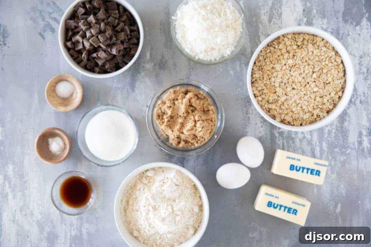Arrangement of ingredients on a white surface, showcasing butter, sugars, eggs, vanilla, salt, baking soda, flour, oats, coconut, and chocolate chunks for Chocolate Chunk Oatmeal Coconut Cookies.