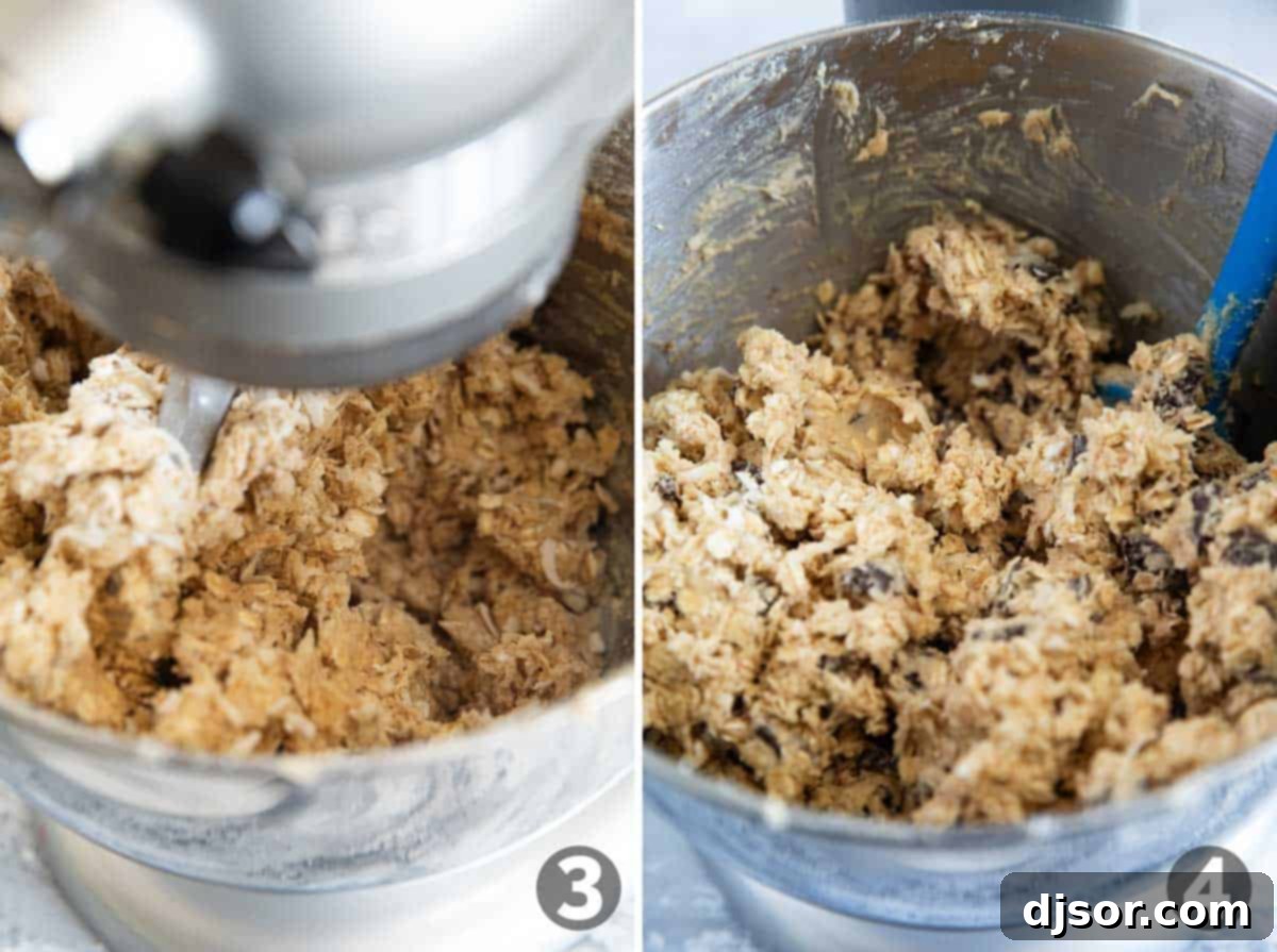 Thick cookie dough in a stand mixer bowl, being mixed with a spatula, with oats, coconut, and chocolate chunks visible.