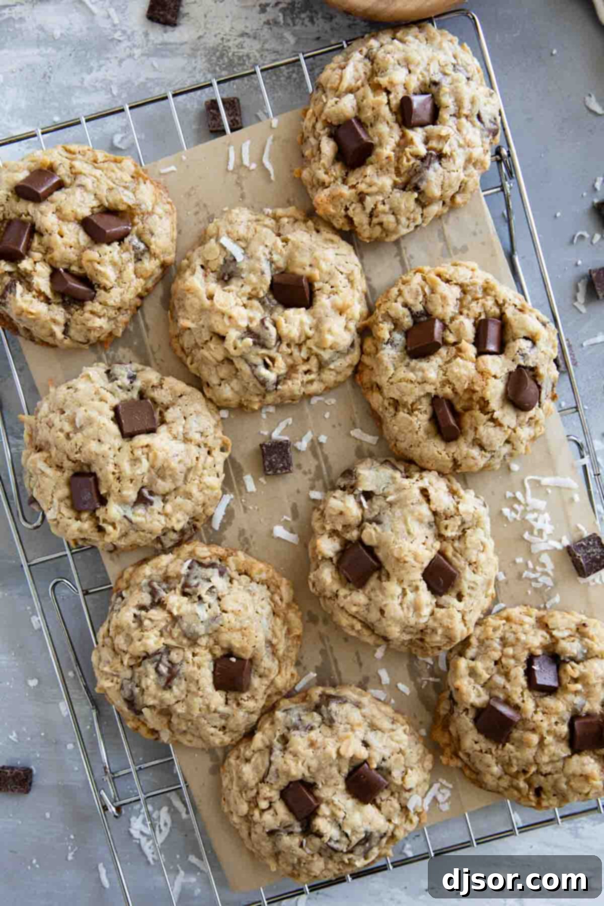 A batch of warm, golden brown Chocolate Chunk Oatmeal Coconut Cookies cooling on a metal wire rack.