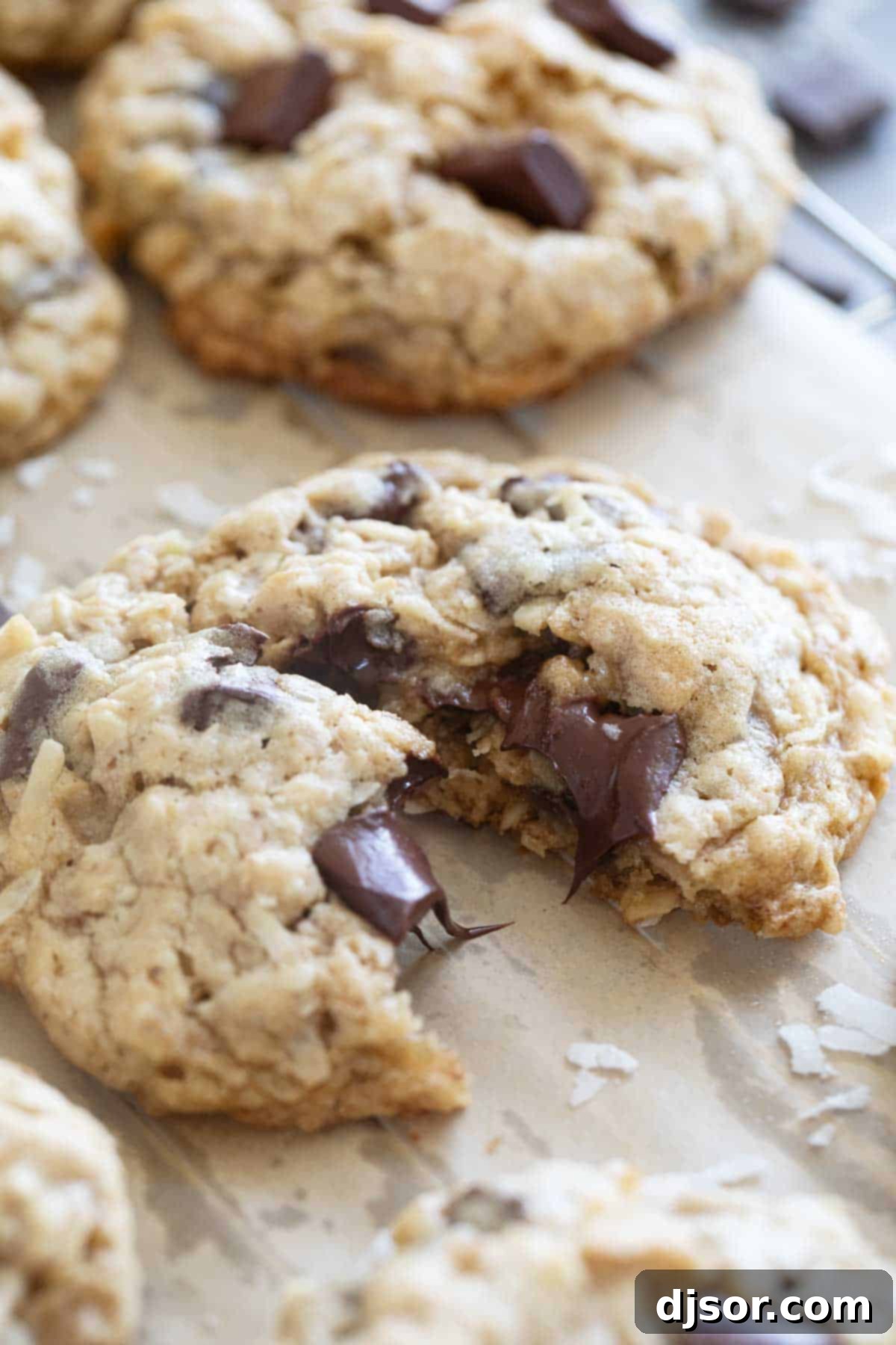 A Chocolate Chunk Oatmeal Coconut Cookie torn in half, showing the warm, melted chocolate and soft, chewy texture inside.