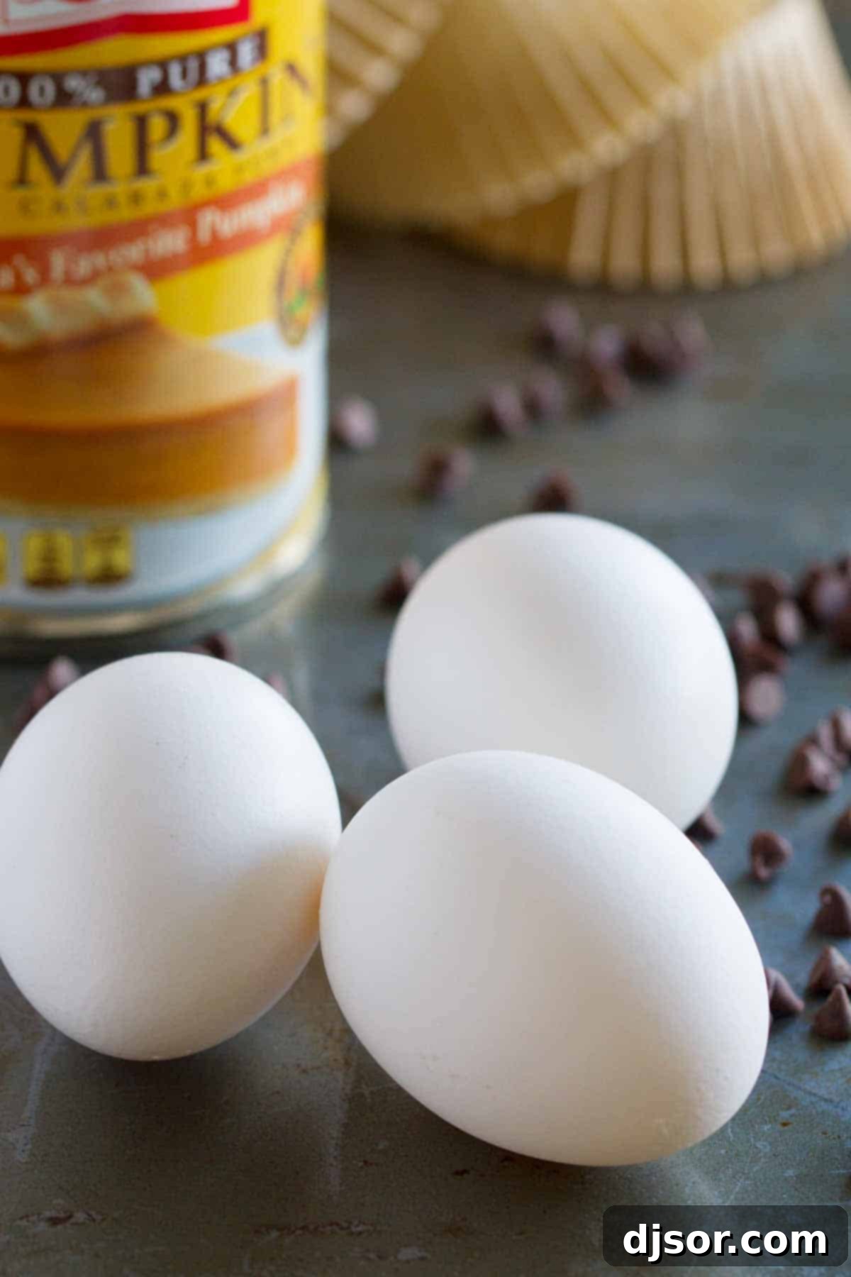 Various ingredients for Pumpkin Cheesecake Spider Cupcakes, including pumpkin puree, eggs, flour, and spices, laid out on a kitchen counter.
