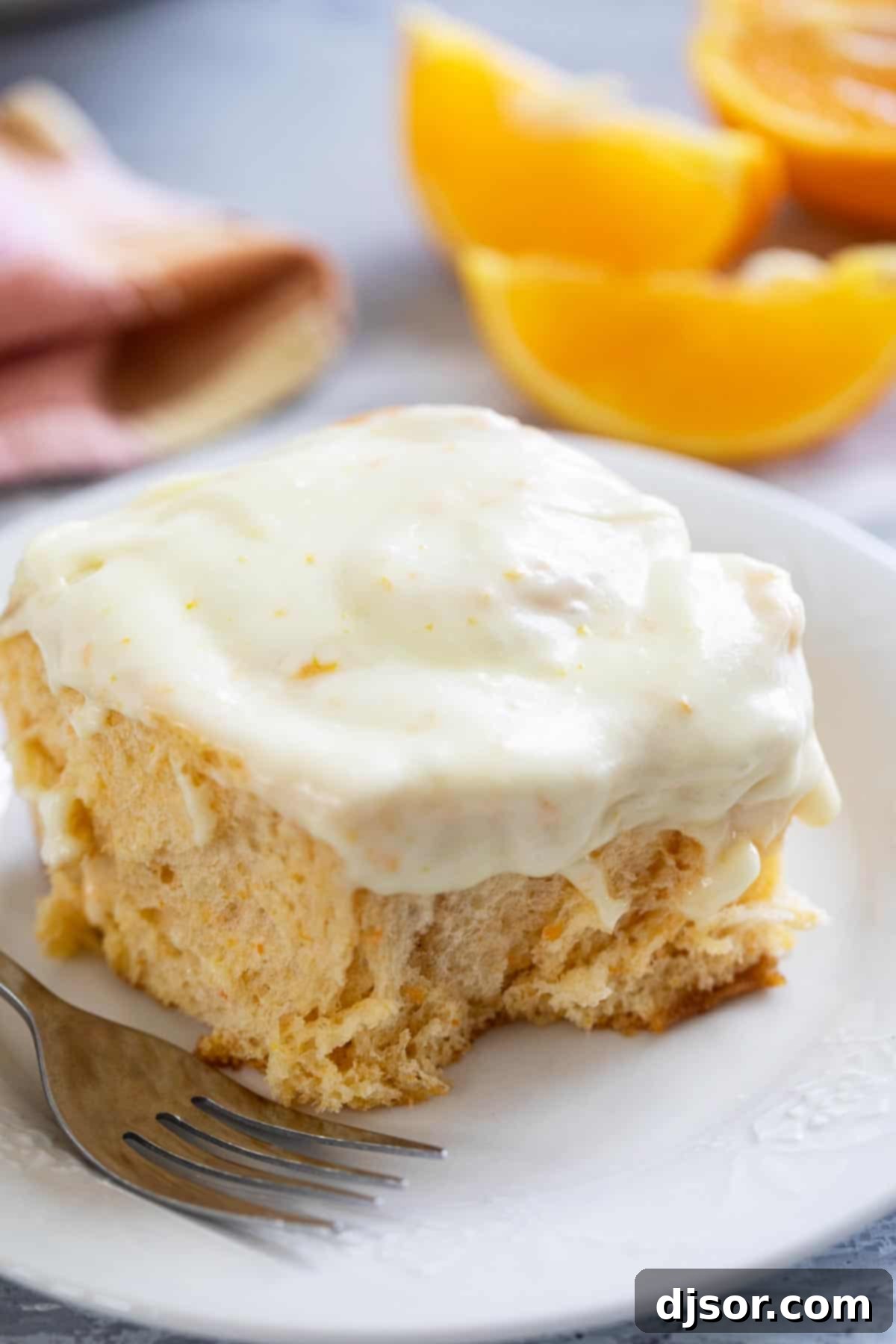 Sweet Potato Cinnamon Roll on a plate, topped with orange cream cheese frosting, with a bite taken with a fork.