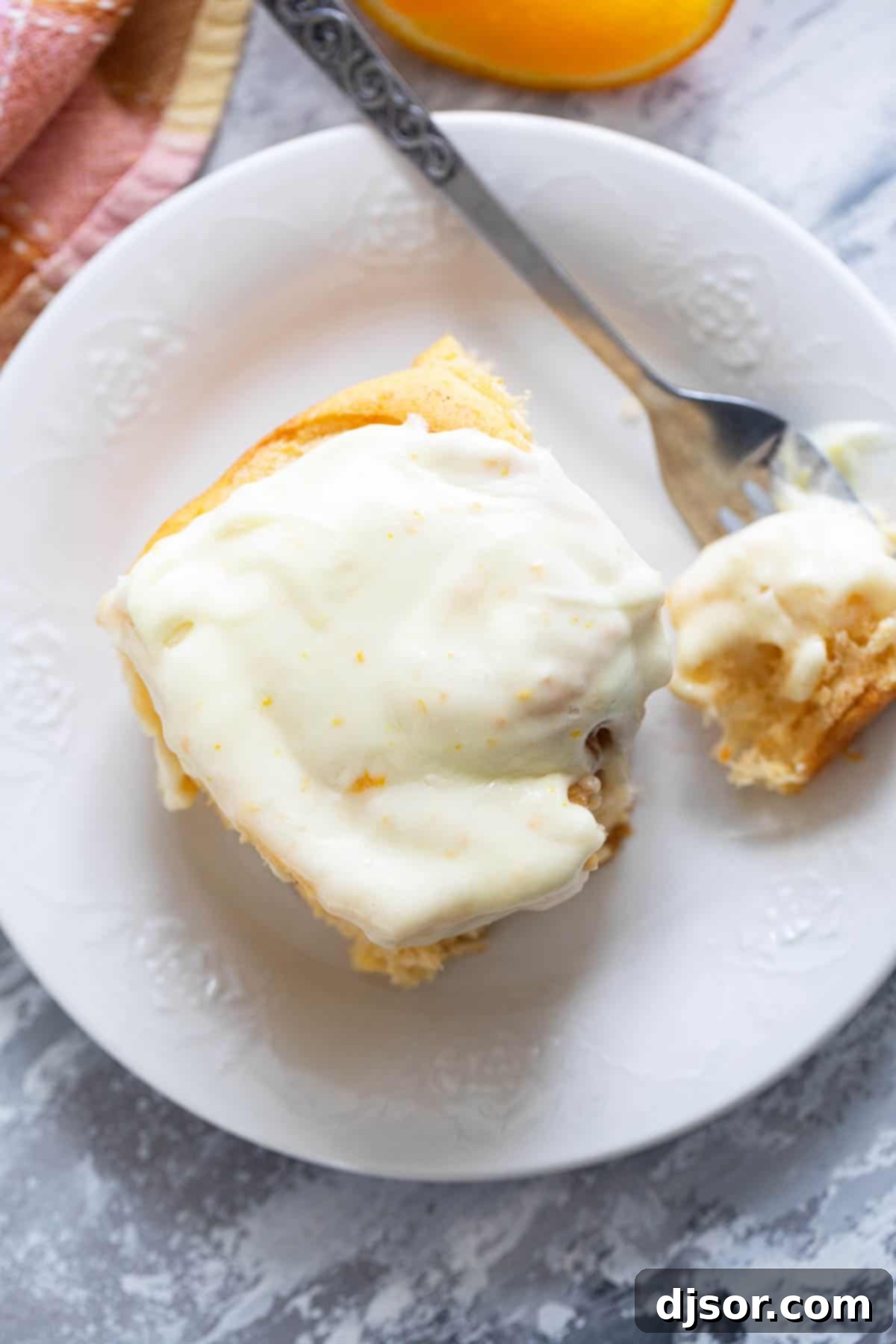 Sweet Potato Cinnamon Roll on a plate, topped with orange cream cheese frosting, with a bite taken with a fork.