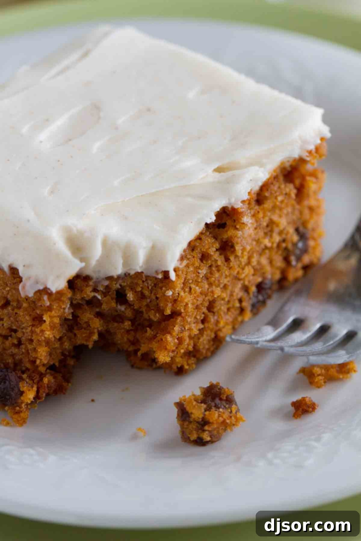 A slice of tomato soup cake with cream cheese frosting, with a bite taken out to reveal its moist, spiced interior.