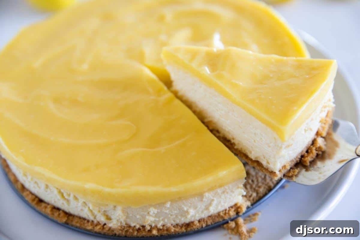 A hand gently lifting a perfect slice of Lemon Cheesecake from the main cake, showcasing its creamy texture and the vibrant lemon curd topping.
