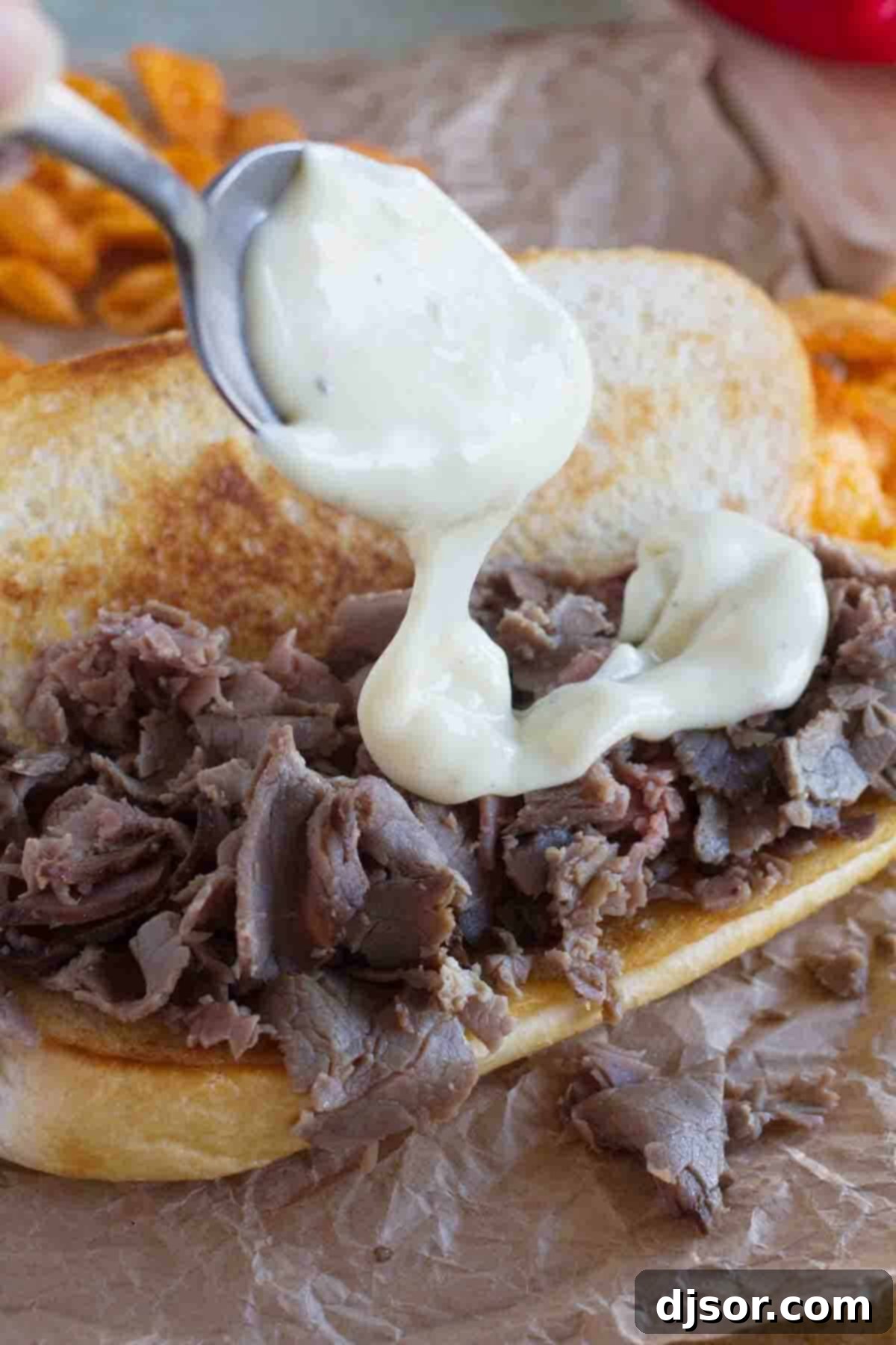 Close-up shot of creamy cheese sauce being generously poured over a bed of tender roast beef for a cheesesteak sandwich, highlighting the rich texture.