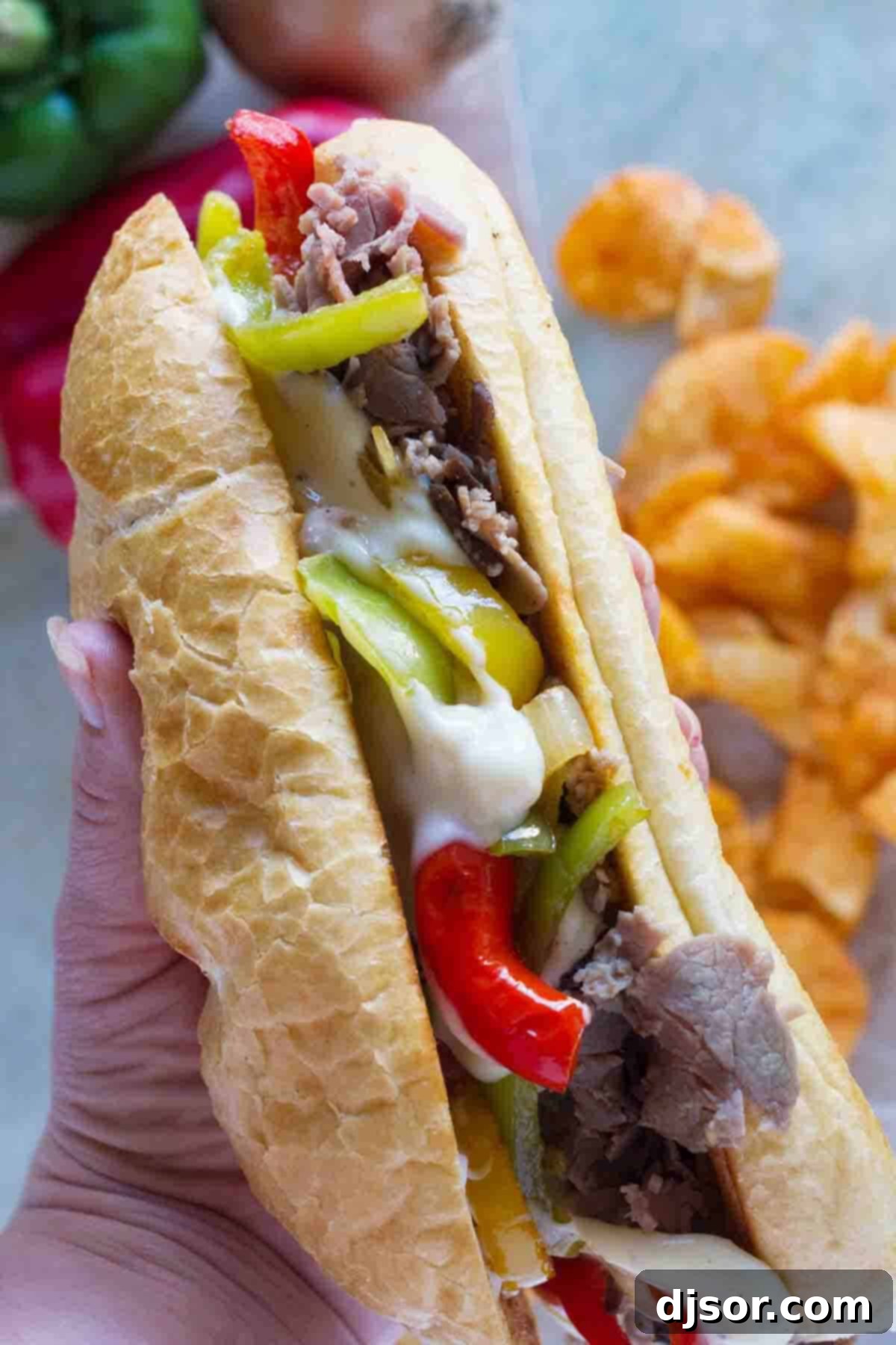 A hand holding a delicious 30-minute cheesesteak sandwich, showcasing the generous filling of roast beef, melted cheese, and colorful peppers and onions spilling out, ready for a bite.