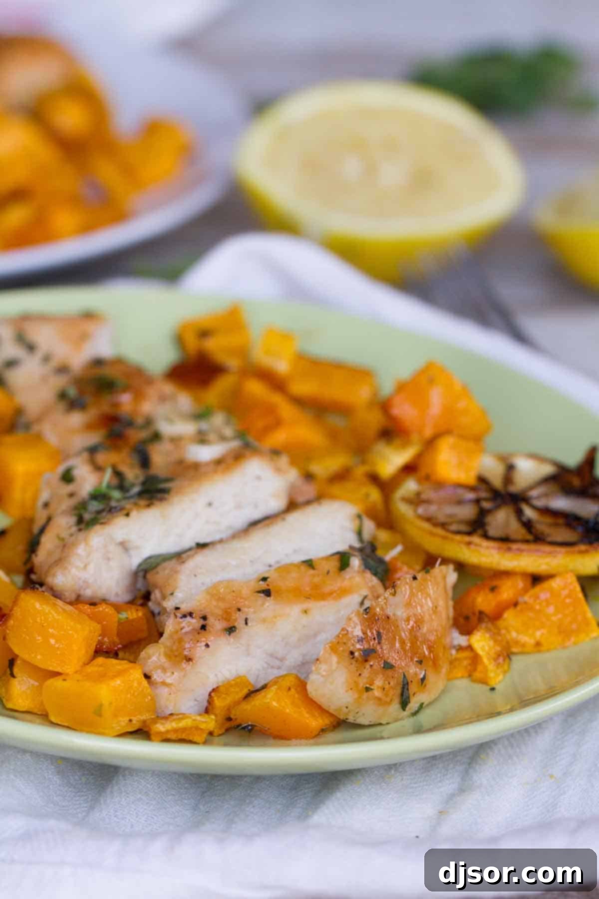 Flavorful Lemon Chicken and Butternut Squash Close-up of sliced lemon chicken breast with roasted butternut squash and lemon wedges on a white plate, highlighting a healthy, flavorful meal.