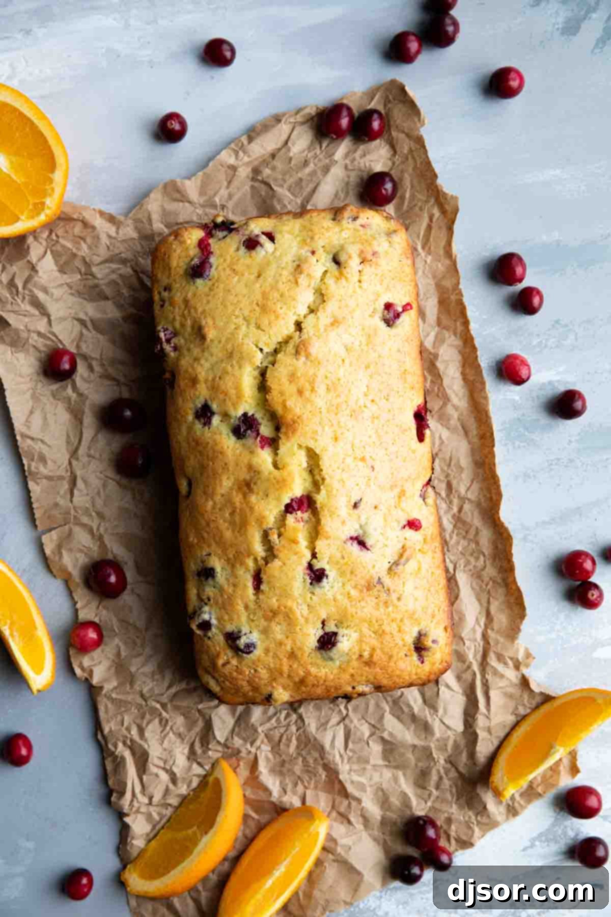 full loaf of cranberry orange bread, garnished with fresh cranberries and orange slices on a wooden board