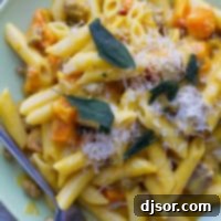 Plate filled with Penne with Butternut Squash and Sausage and topped with parmesan cheese and sage.