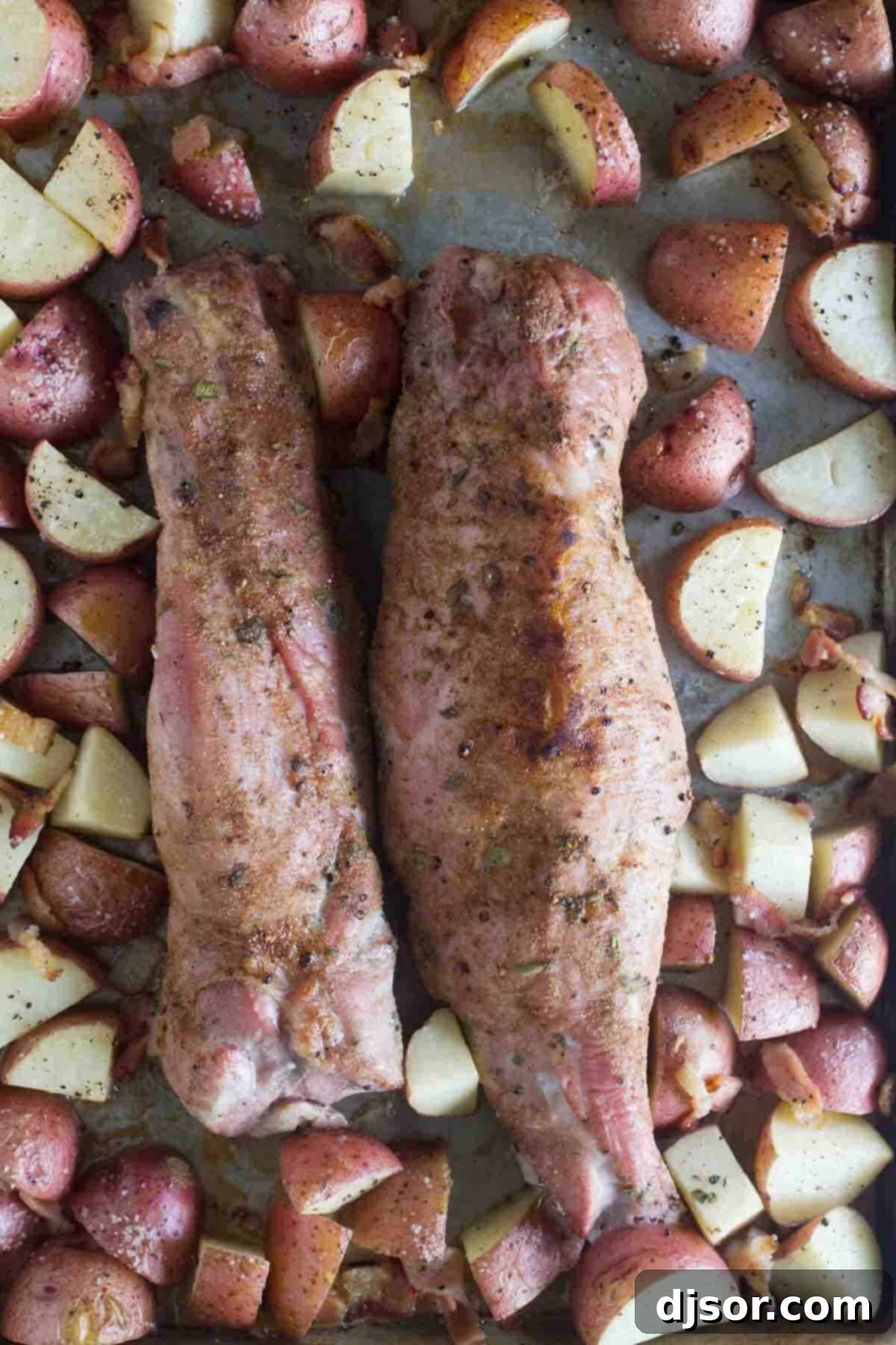 Two seasoned pork tenderloins and chopped baby red potatoes, mixed with bacon pieces, spread on a baking sheet, ready for roasting.
