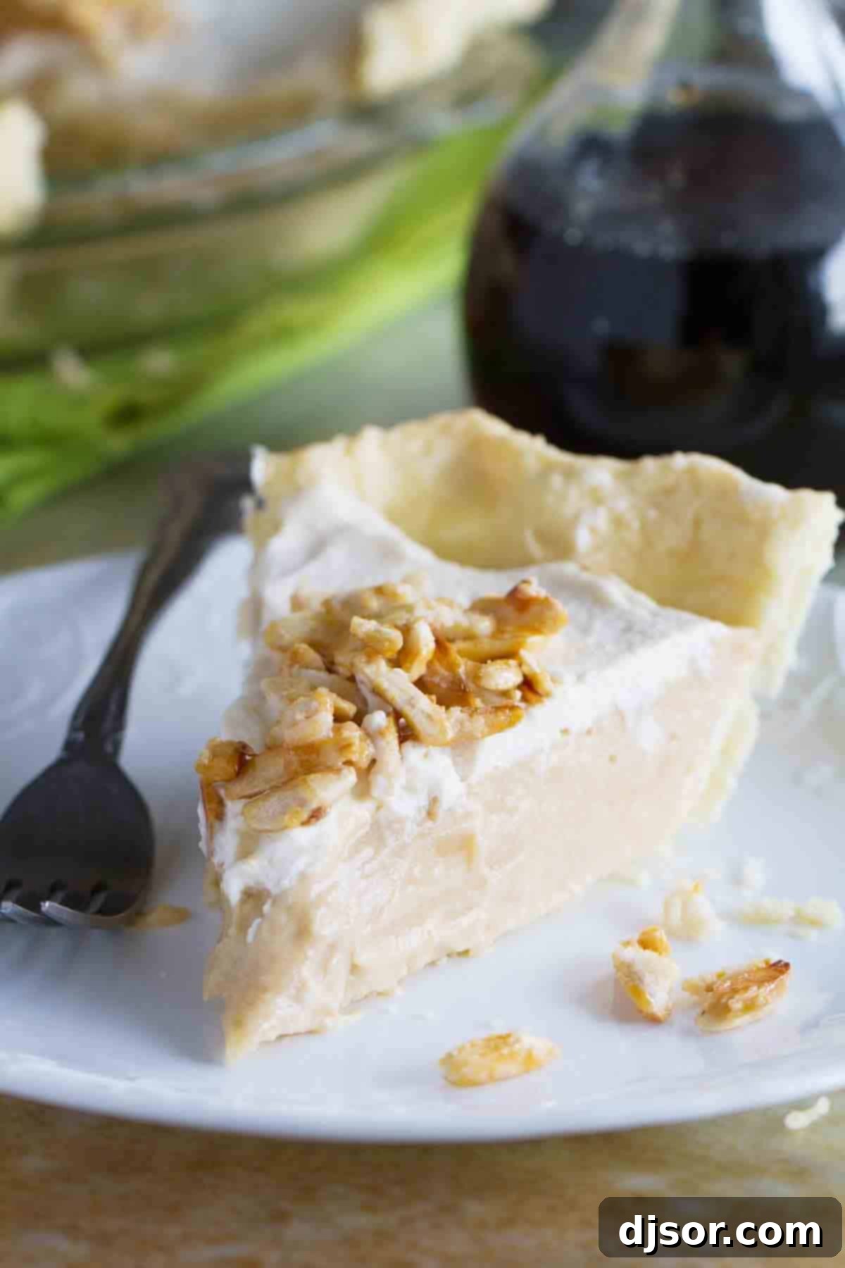 Maple Cream Pie Slice A perfectly sliced piece of Maple Cream Pie, showcasing its creamy filling, fluffy whipped cream, and crunchy sugared almond topping, resting on a white plate, ready to be enjoyed.
