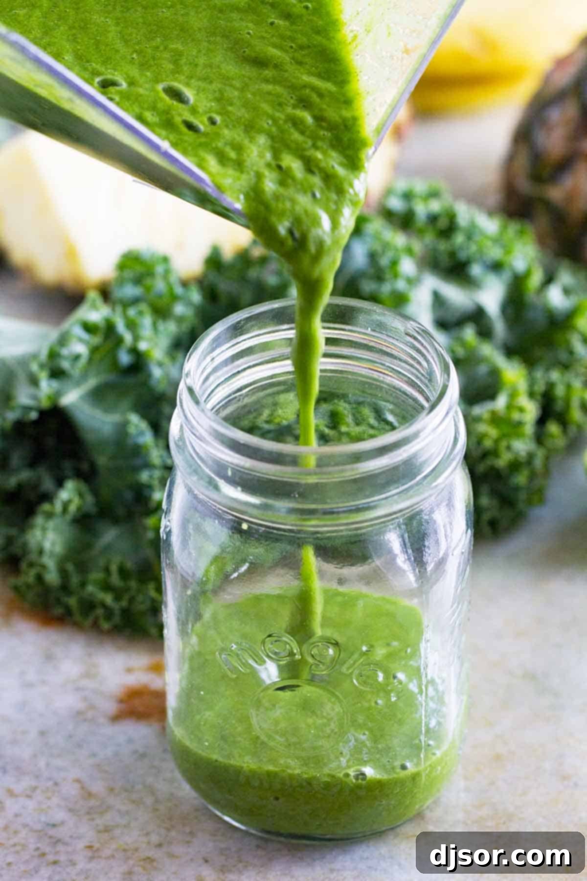 Enjoy pouring this delicious and healthy green smoothie. A stream of freshly blended kale smoothie being poured into a tall glass jar, showcasing its smooth, vibrant green color.