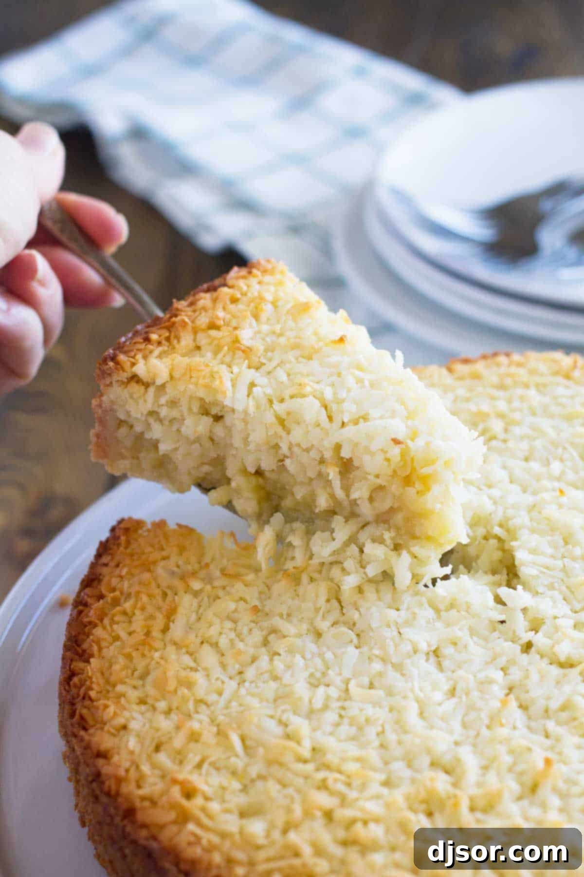 A hand gently takes a slice of freshly baked Coconut Custard Pie from the full pie, revealing its creamy texture.