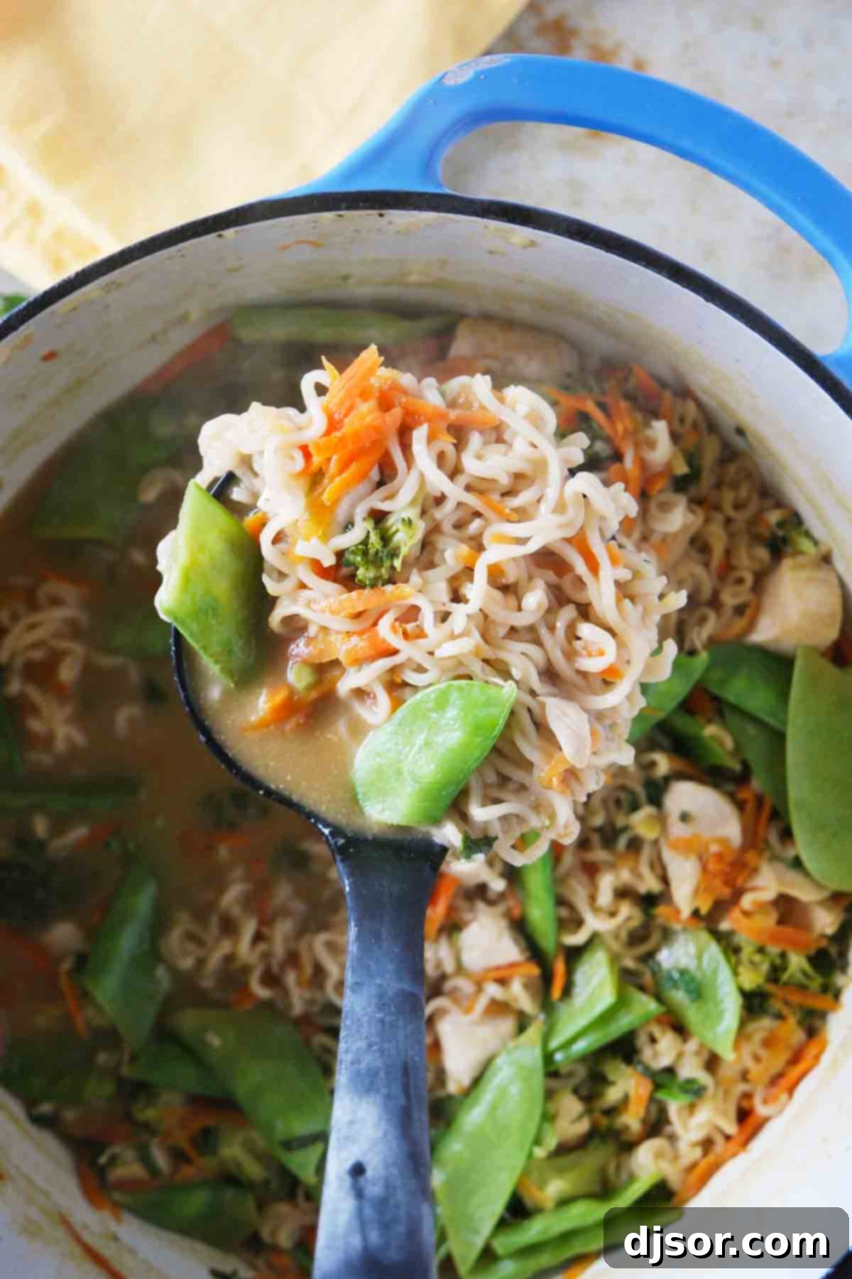 A Dutch oven filled with simmering Asian Chicken Noodle Soup, with a ladle ready to serve, illustrating its rich texture and color.