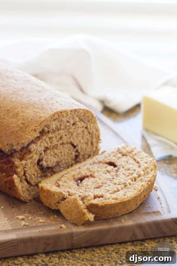A freshly baked loaf of Whole Wheat Cinnamon Swirl Bread with a slice cut, showing the beautiful cinnamon swirl inside.