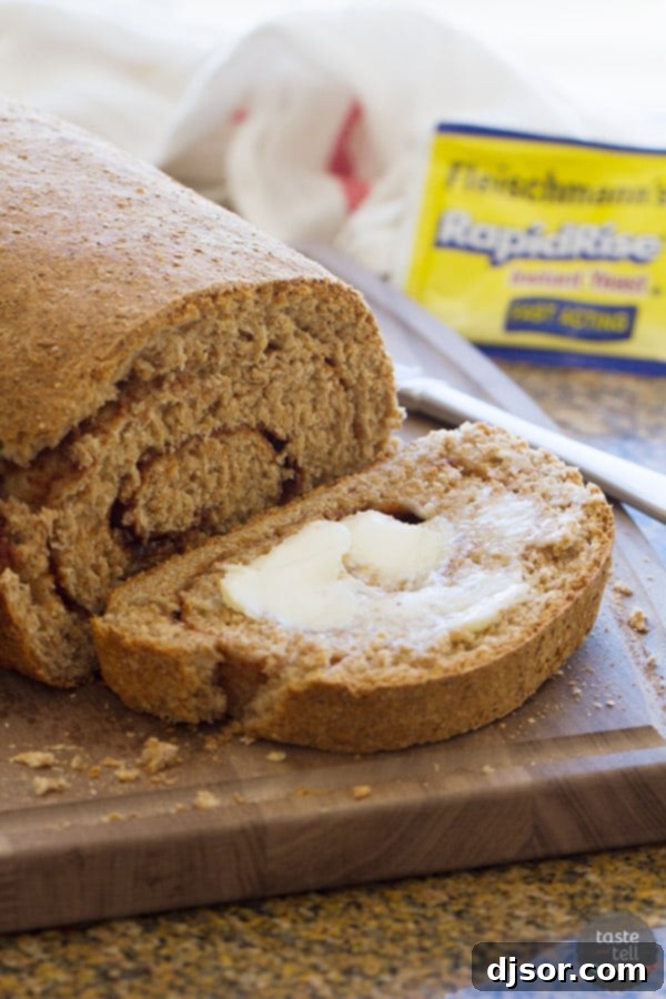 A close-up of a slice of Whole Wheat Cinnamon Swirl Bread with a pat of butter melting on top, on a wooden board.