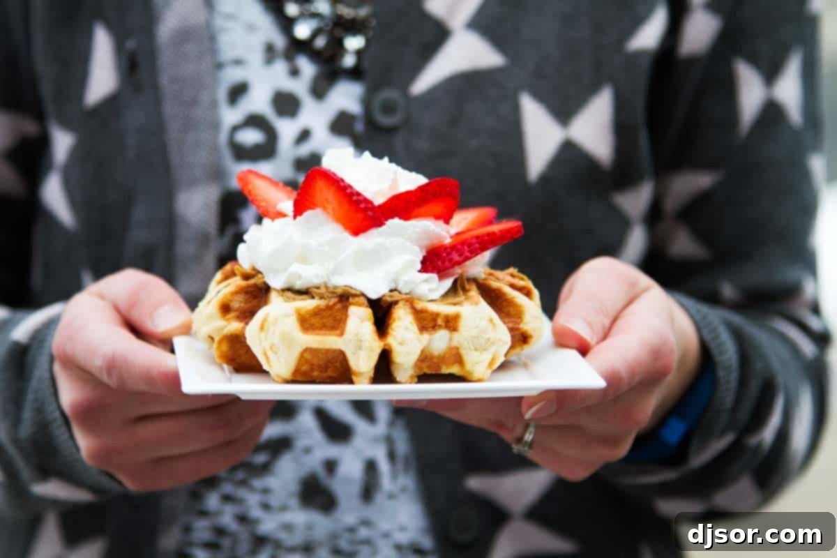 Bring a taste of Belgium into your kitchen with these Liege Waffles! A wonderful special breakfast or afternoon treat, these yeasted sugar waffles are irresistible. A hand holding a plate with a freshly baked Liege waffle, generously topped with fluffy whipped cream and vibrant strawberries.