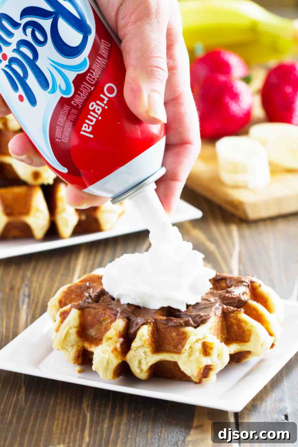 Bring a taste of Belgium into your kitchen with these Liege Waffles! A wonderful special breakfast or afternoon treat, these yeasted sugar waffles are irresistible. A close-up of a warm Liege waffle being generously topped with fresh whipped cream and ripe strawberries.