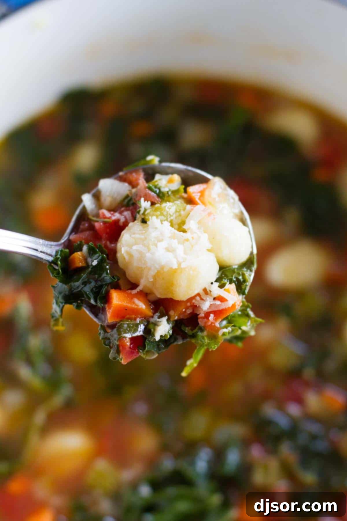 A ladle scooping a generous portion of Minestrone with Gnocchi from a large pot, highlighting the rich broth and diverse ingredients.