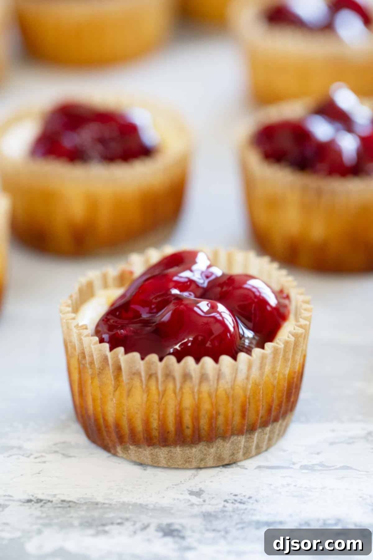 Beautifully baked mini cheesecakes in muffin tins, each generously topped with bright red cherries, ready to be enjoyed.