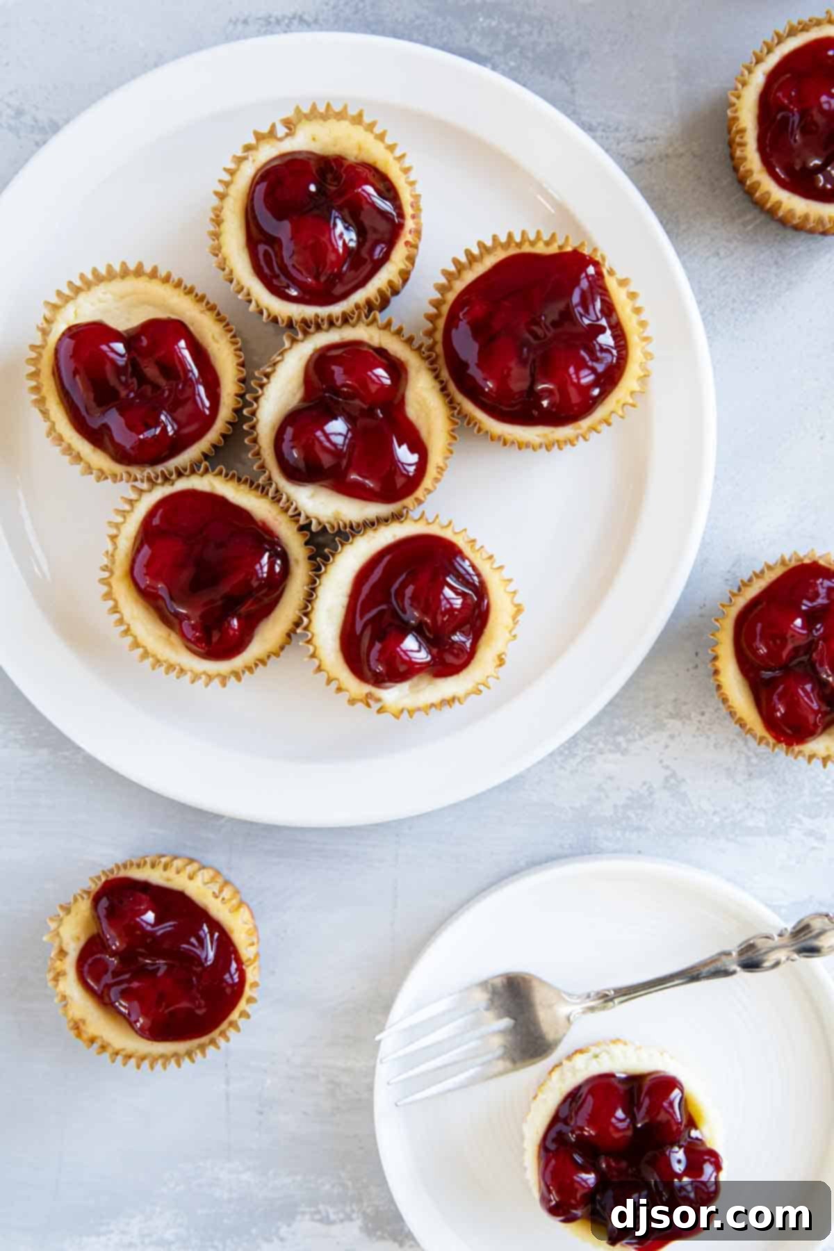 Individual mini cheesecakes, perfectly portioned and exquisitely topped with glistening cherry pie filling, presented on plates, ready to be served.