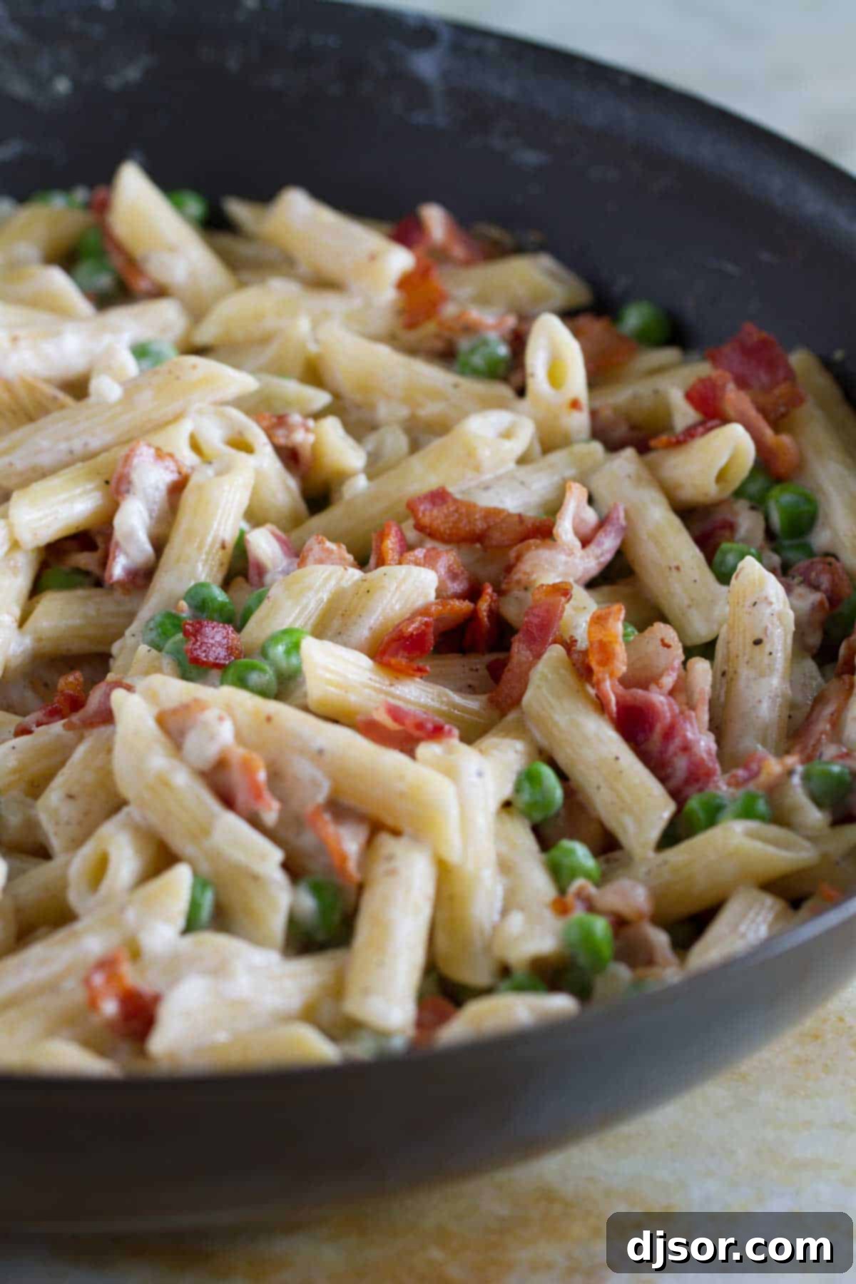 Smoky Bacon Sweet Pea Skillet Pasta 3 Close-up shot of creamy pasta mixed with crispy bacon and bright green peas, simmering in a large skillet on the stovetop.