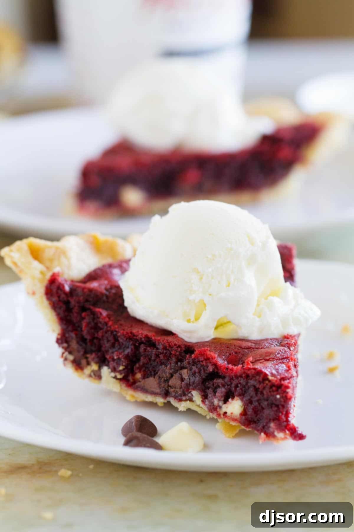 A delectable slice of Red Velvet Cookie Pie, generously topped with a melting scoop of vanilla ice cream, promising a perfect blend of warm and cold textures.