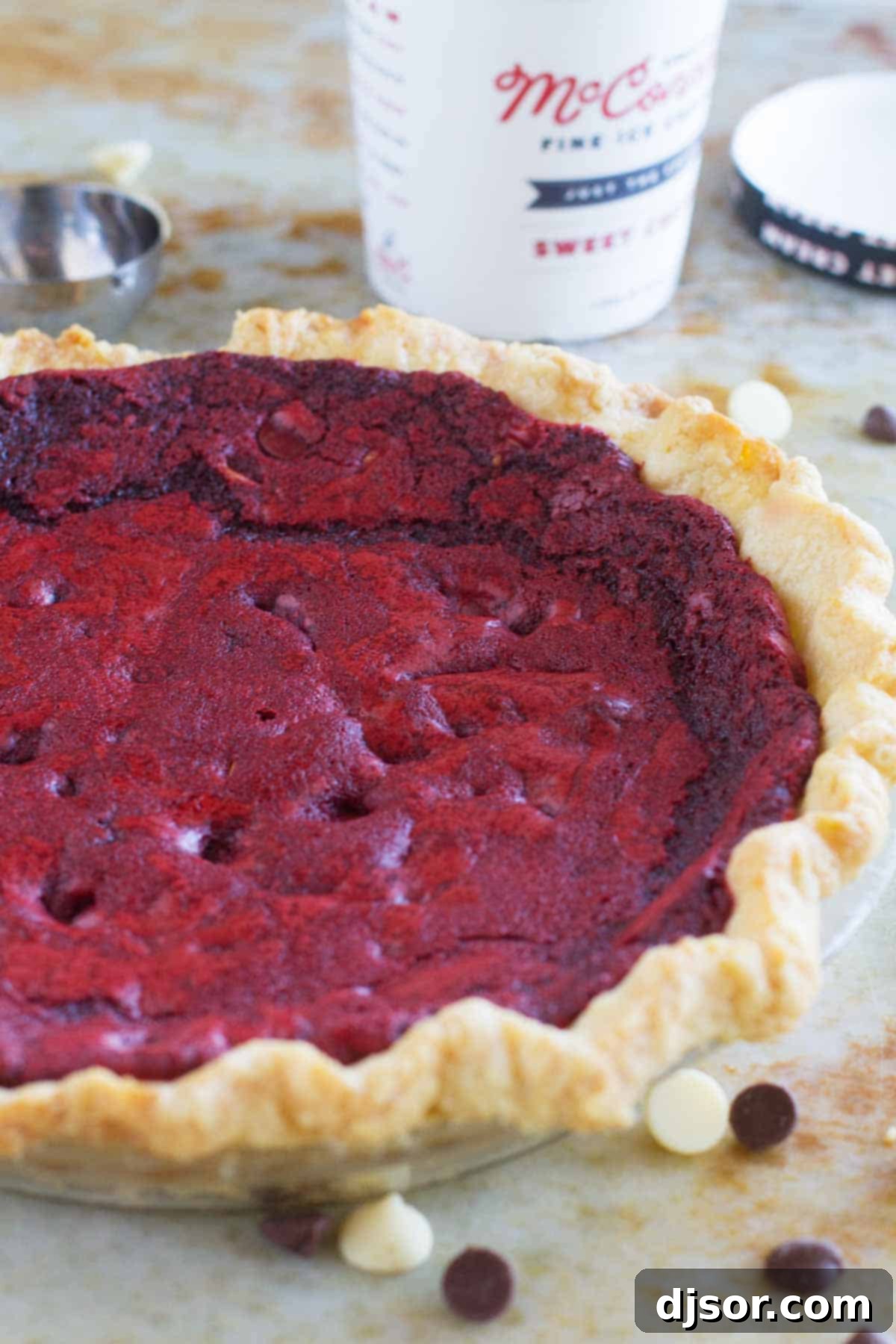 A vibrant, full Red Velvet Cookie Pie proudly displayed, with a pint of creamy ice cream subtly blurred in the background, hinting at its perfect pairing.