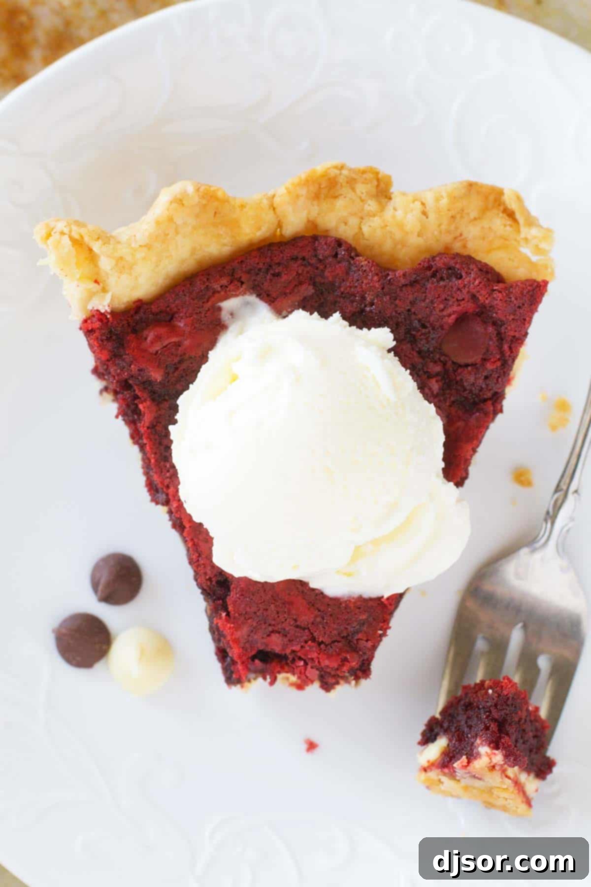 A perfectly portioned slice of Red Velvet Cookie Pie, showing its rich, red interior and tender crust, with a tantalizing bite already taken, inviting indulgence.