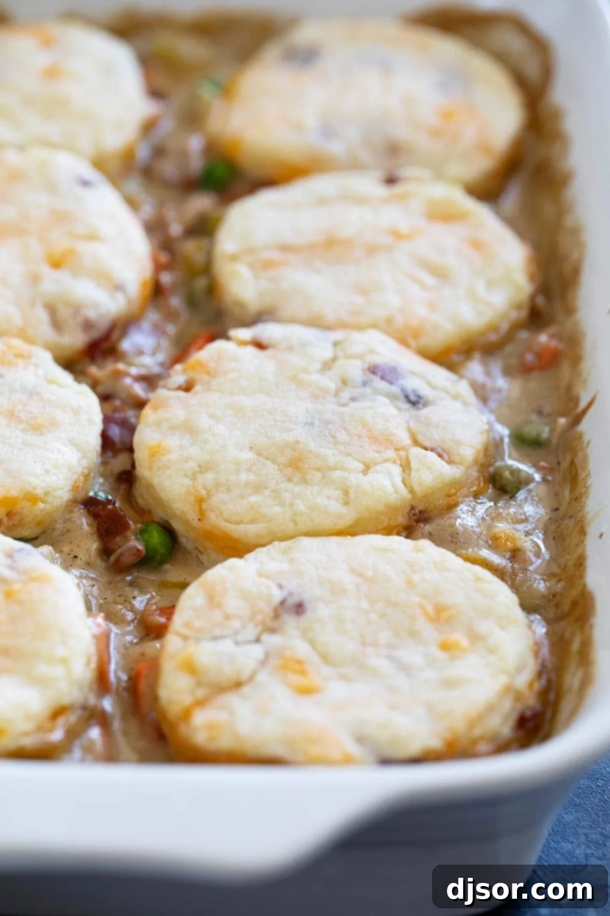 A golden-brown chicken pot pie with fluffy bacon cheddar biscuits in a white casserole dish, ready to be served.
