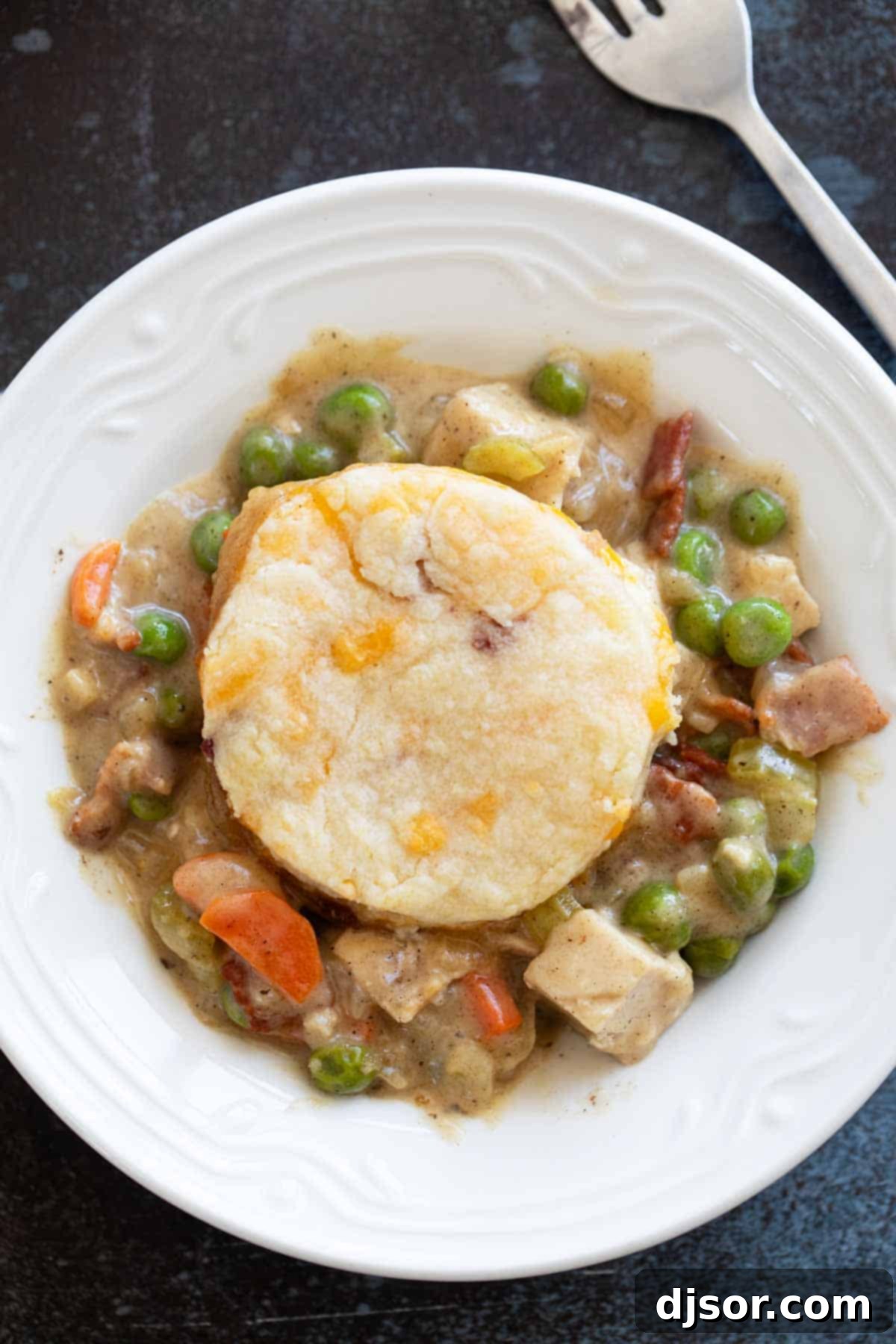 A serving of Chicken Pot Pie with Biscuits and Bacon in a shallow bowl, showcasing the creamy filling and golden biscuit topping.