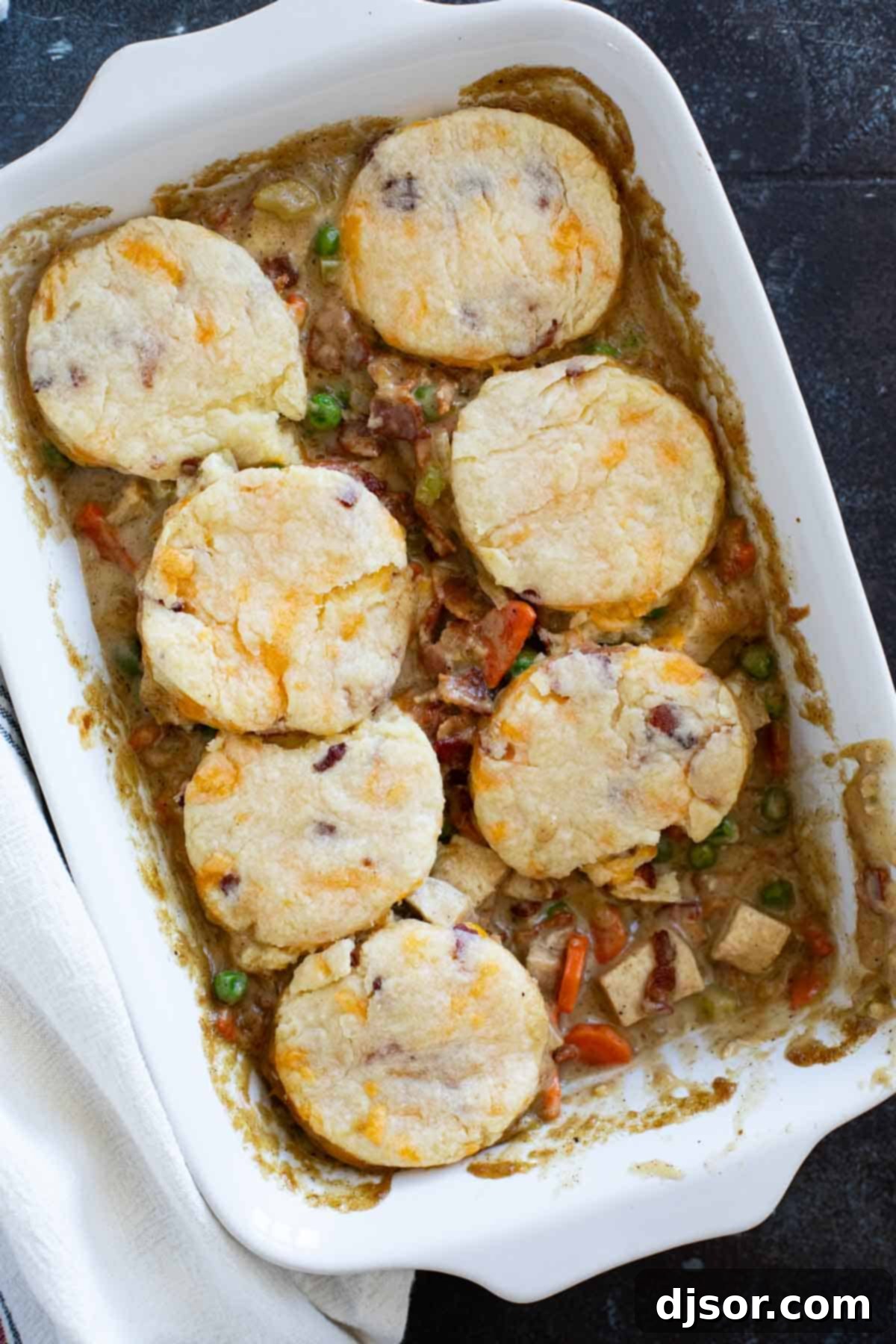 A casserole dish with Chicken Pot Pie with Bacon and Biscuits, with a portion removed to reveal the creamy filling.