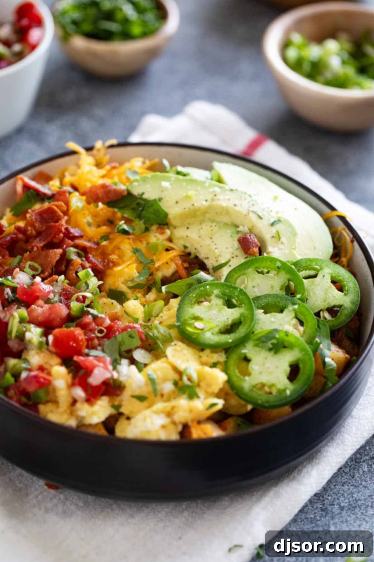 Loaded breakfast bowl, with roasted potatoes, scrambled eggs, bacon, and lots of toppings, ready to be enjoyed.