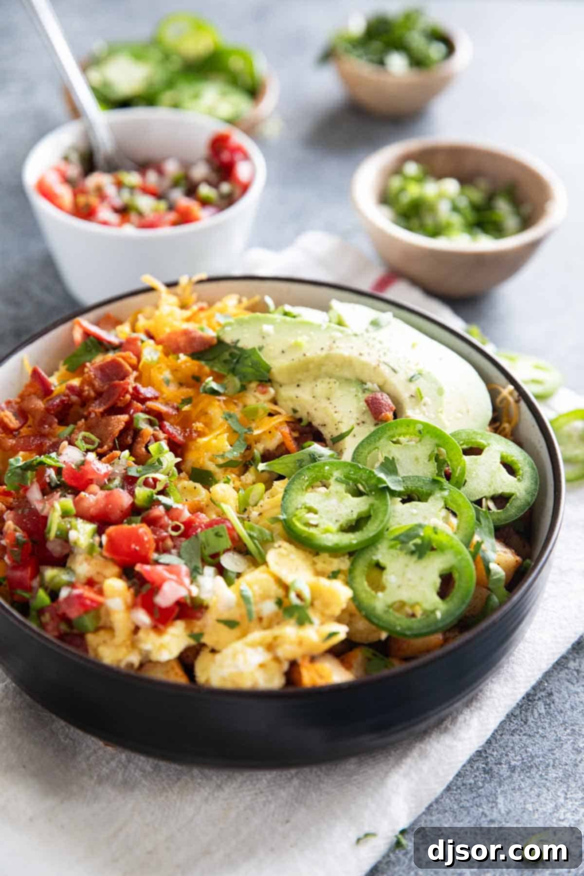 A breakfast bowl with a focus on fresh toppings, with small bowls of various condiments and garnishes blurred in the background, suggesting a customizable meal.
