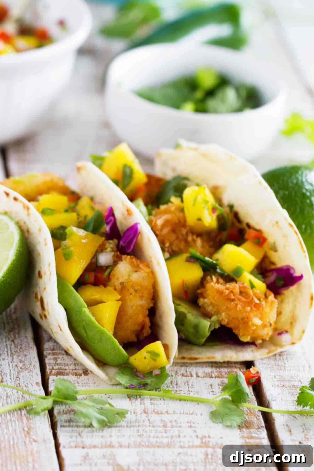 Two coconut shrimp tacos topped with mango salsa and avocado, ready to be enjoyed.