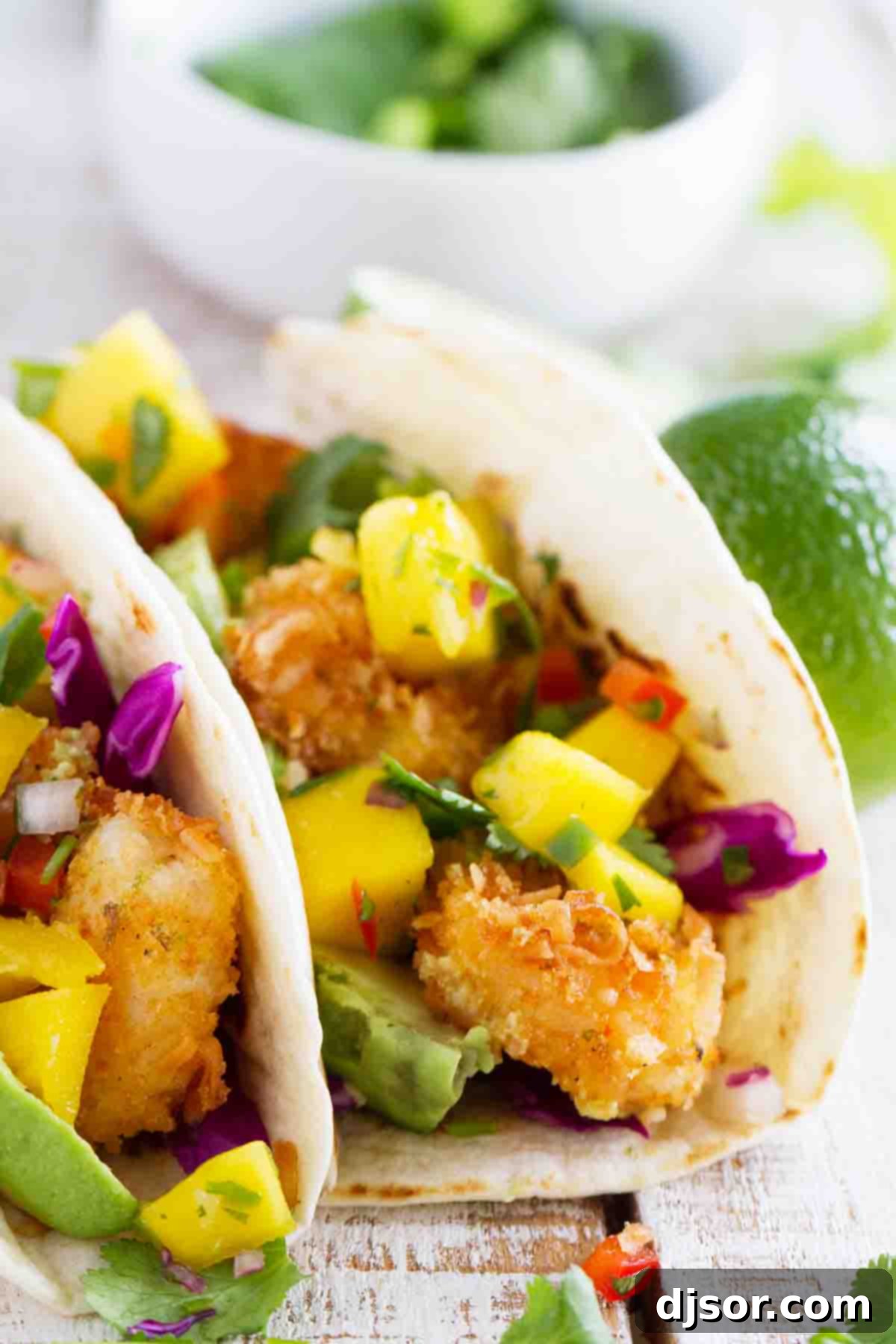 A close-up of a Coconut Shrimp Taco, showing the texture of the crispy shrimp and the vibrant colors of the mango salsa and avocado slices.