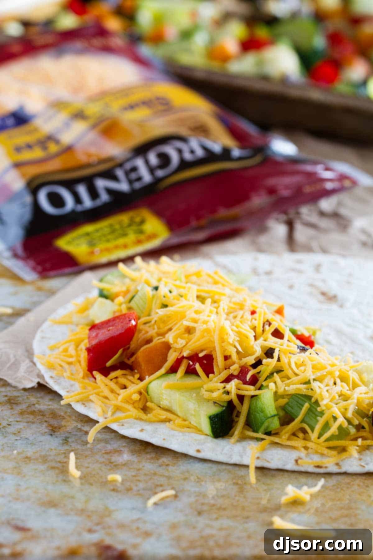 A close-up shot of a tortilla being filled with generous amounts of shredded cheese and a colorful mix of perfectly roasted vegetables, ready to be folded.