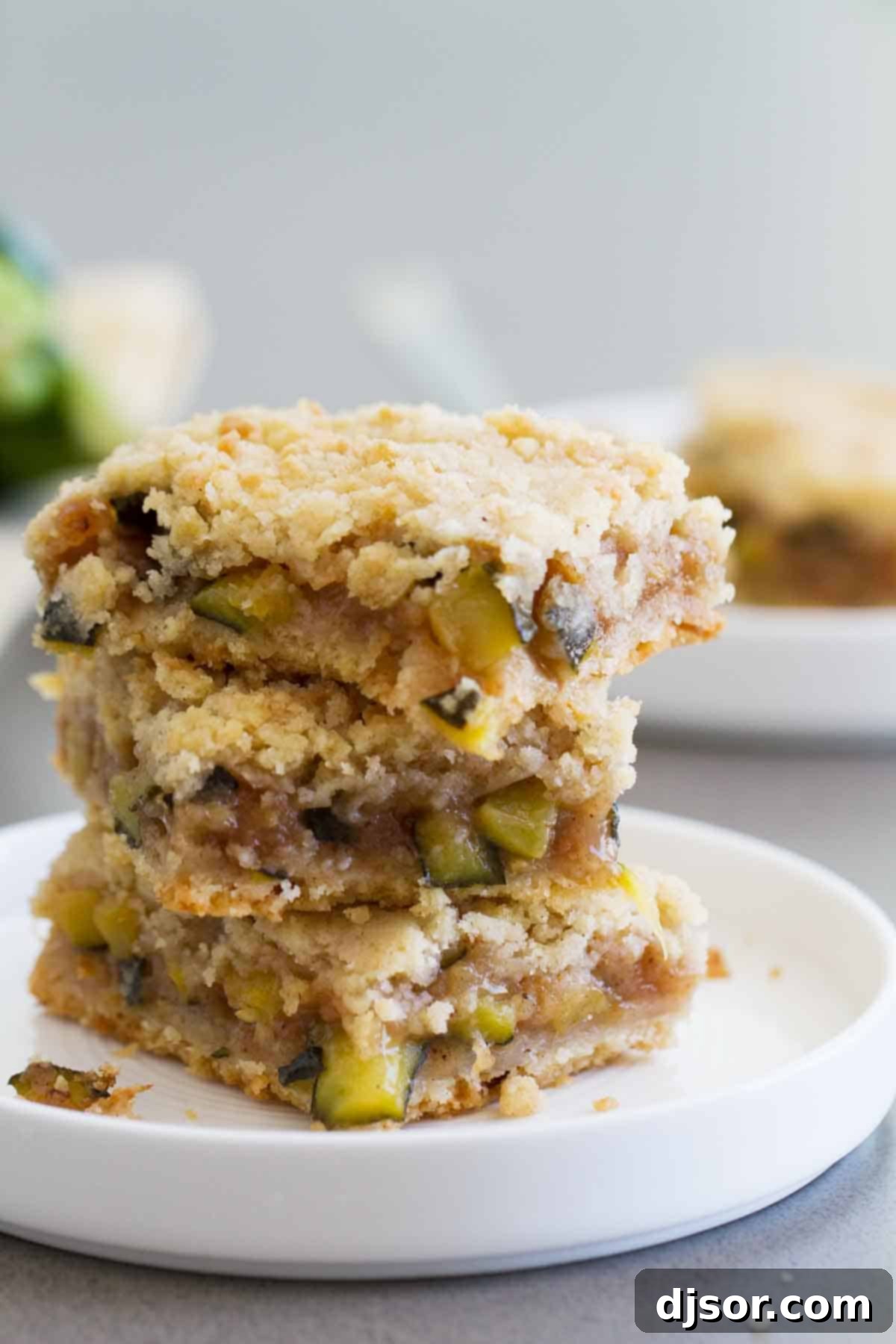Zucchini Cobbler Bars: A sweet and surprising treat perfect for any occasion. Three golden brown Zucchini Cobbler Bars stacked neatly on a white surface, highlighting their crumbly topping and inviting texture.