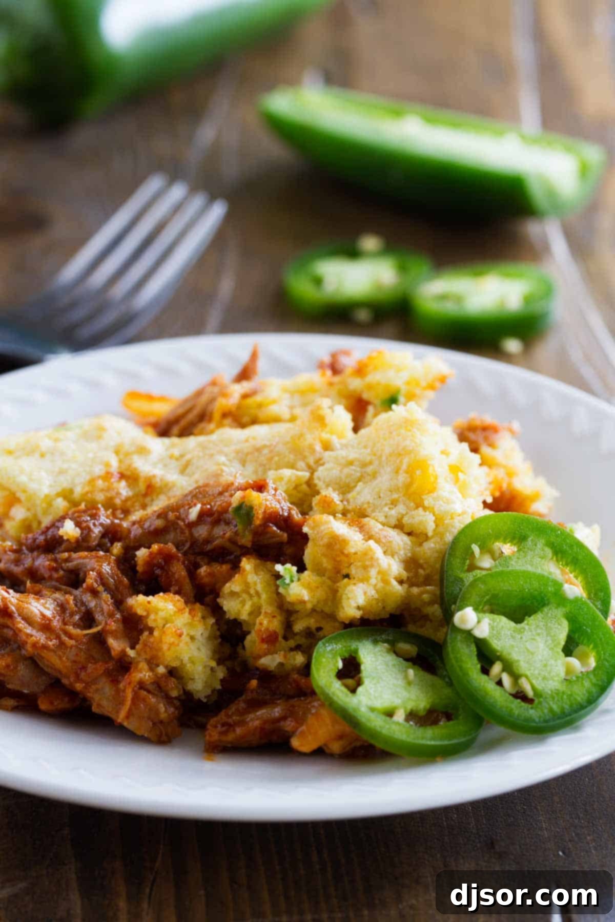 Cornbread-Crusted BBQ Pork Casserole 4 A plate featuring a generous serving of Cornbread Topped BBQ Pork, garnished with fresh sliced jalapeños.