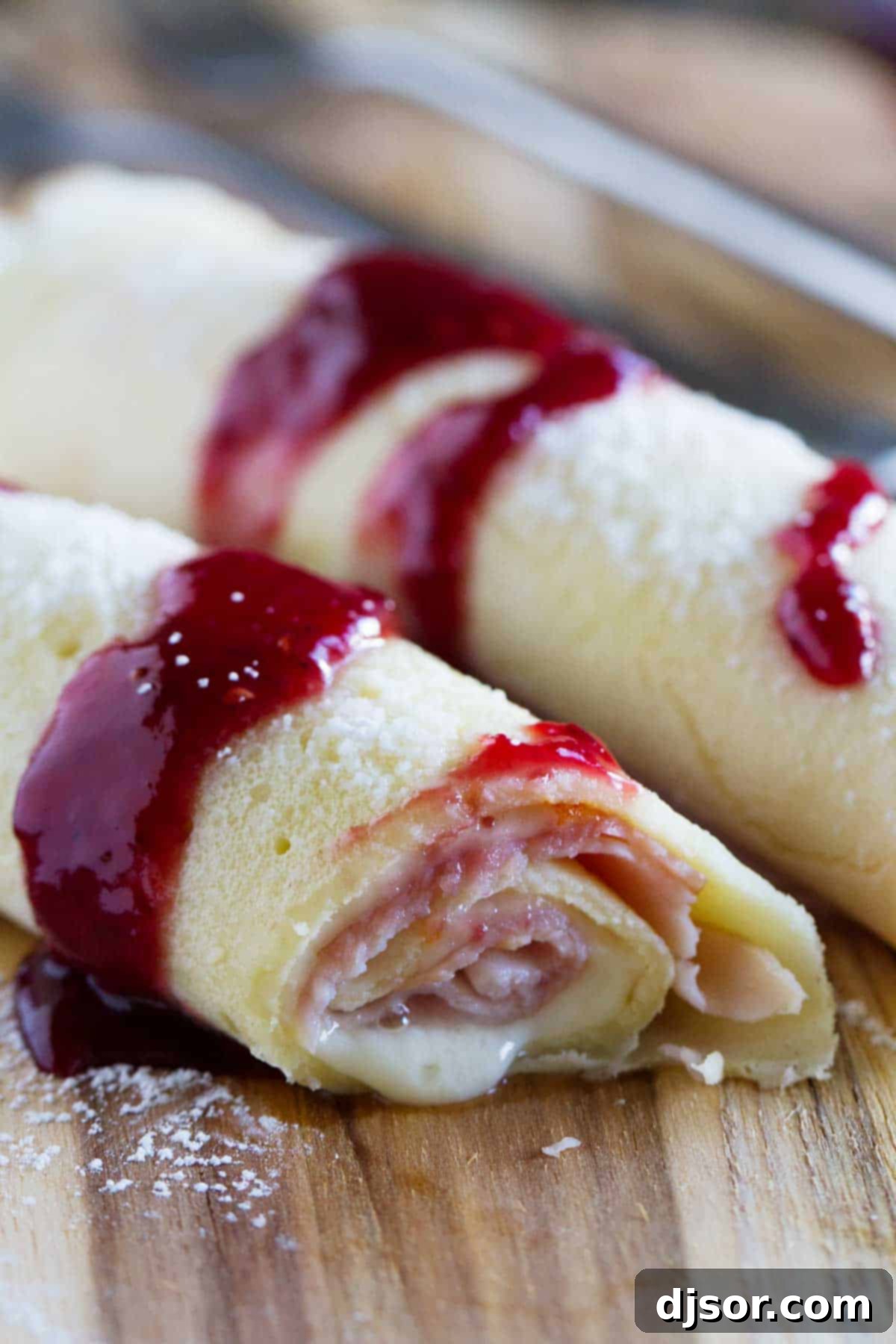 A close-up of a Monte Cristo Crepe, beautifully golden with a hint of raspberry jam and powdered sugar, promising a delightful sweet and savory experience.