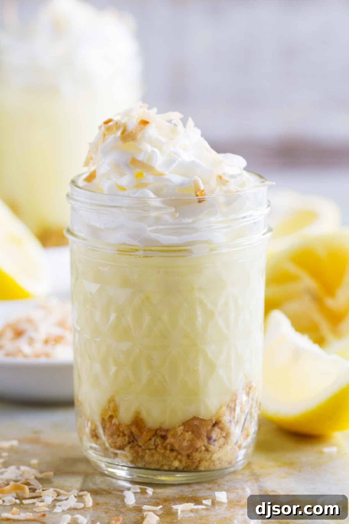A charming glass jar filled with luscious Coconut Lemon Pudding Parfait, generously topped with a swirl of whipped cream and a sprinkle of toasted coconut.