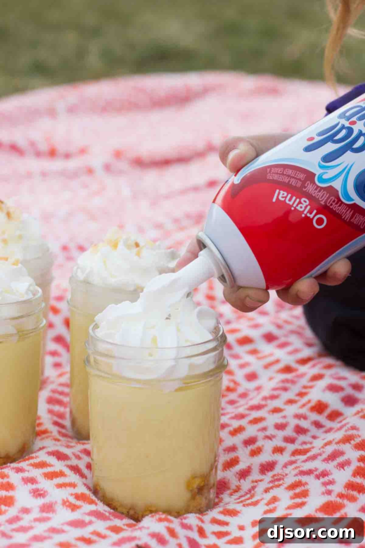 A close-up shot of a Coconut Lemon Pudding Parfait being topped with a perfect swirl of Reddi-wip whipped cream, highlighting its creamy texture.