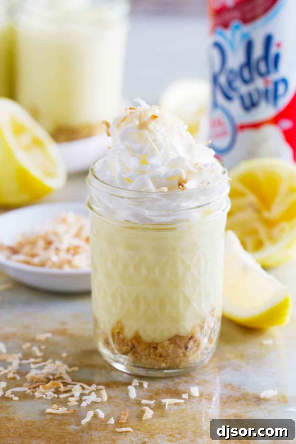 A close-up of a jar showcasing the layers: crushed cookies, creamy homemade lemon pudding, fluffy whipped cream, and a sprinkle of toasted coconut.