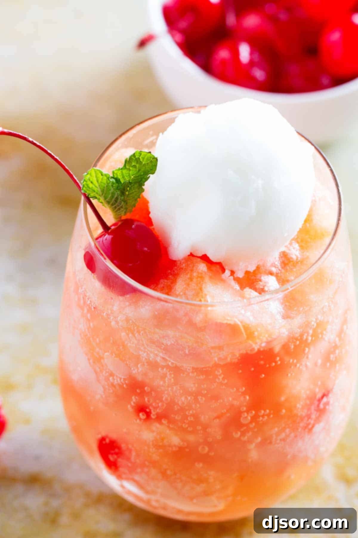 close up of fruit freeze topped with sorbet and a cherry, garnished with fresh mint.