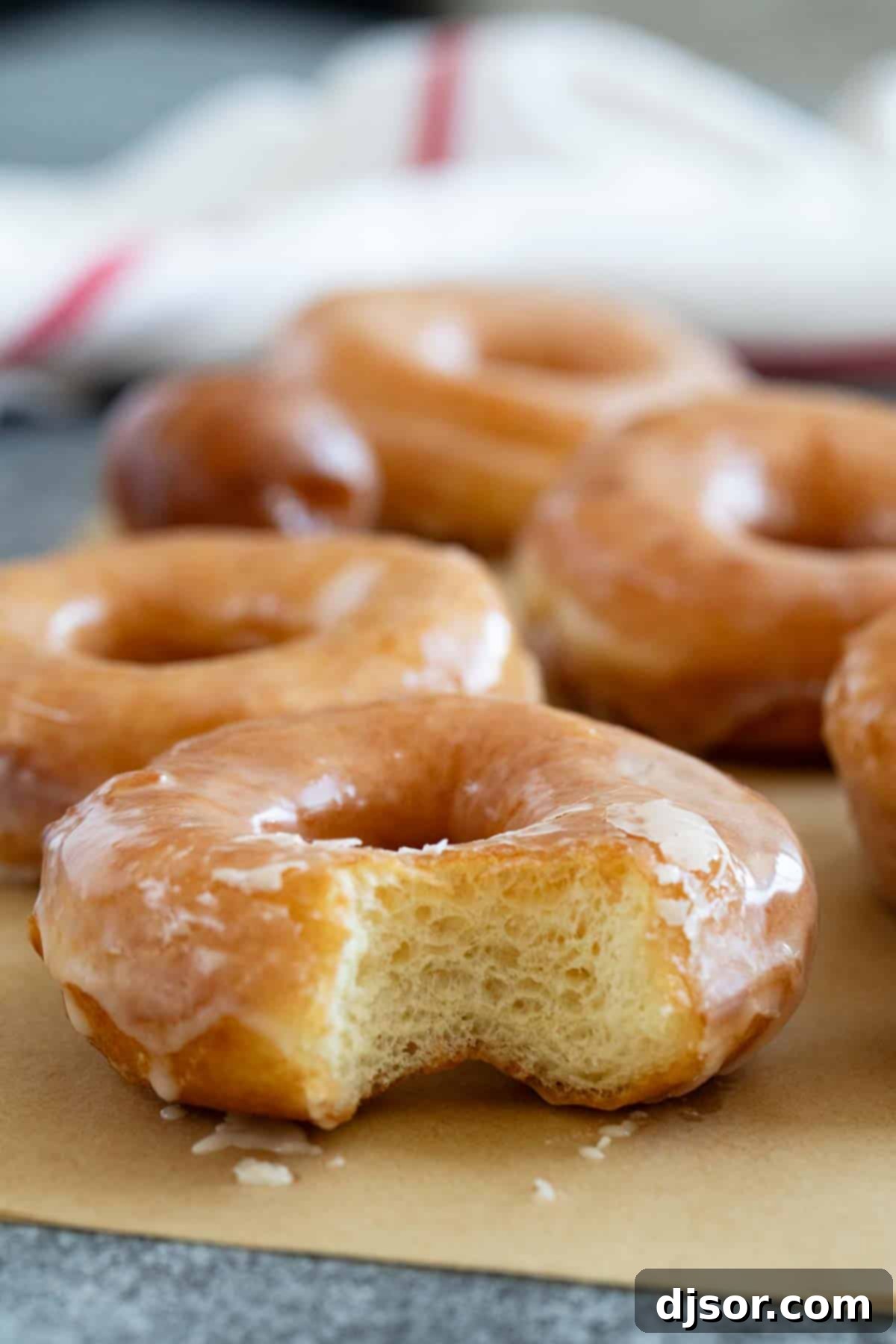 Classic Glazed Delights 9 A close-up shot of a homemade glazed donut with a bite taken out, revealing its fluffy interior, alongside other perfectly glazed donuts.