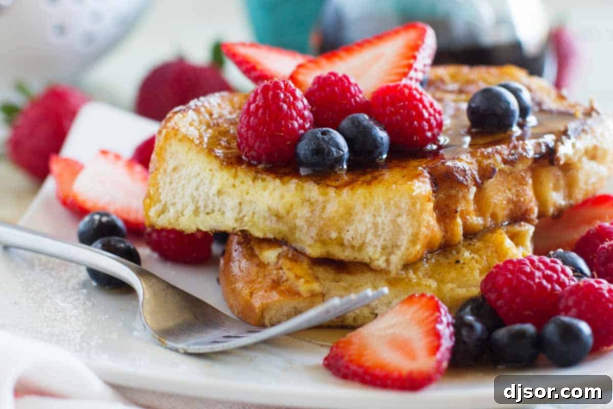 A stack of golden brown Ice Cream French Toast slices topped with fresh berries and maple syrup, set on a white platter. The bread is perfectly soaked and slightly caramelized.