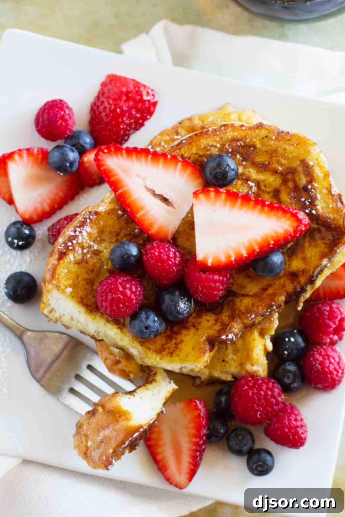 An inviting overhead view of a stack of fluffy Ice Cream French Toast, generously topped with a medley of fresh blueberries, raspberries, and a light dusting of powdered sugar.