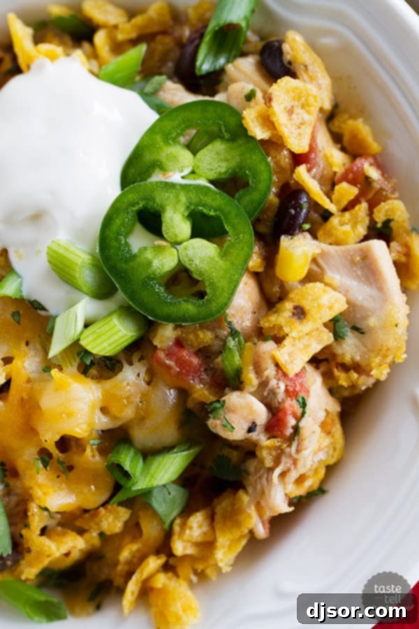 A serving of Slow Cooker Cheesy Chicken and Frito Casserole in a bowl, topped with sour cream and green onions. Ideal for a cozy dinner.