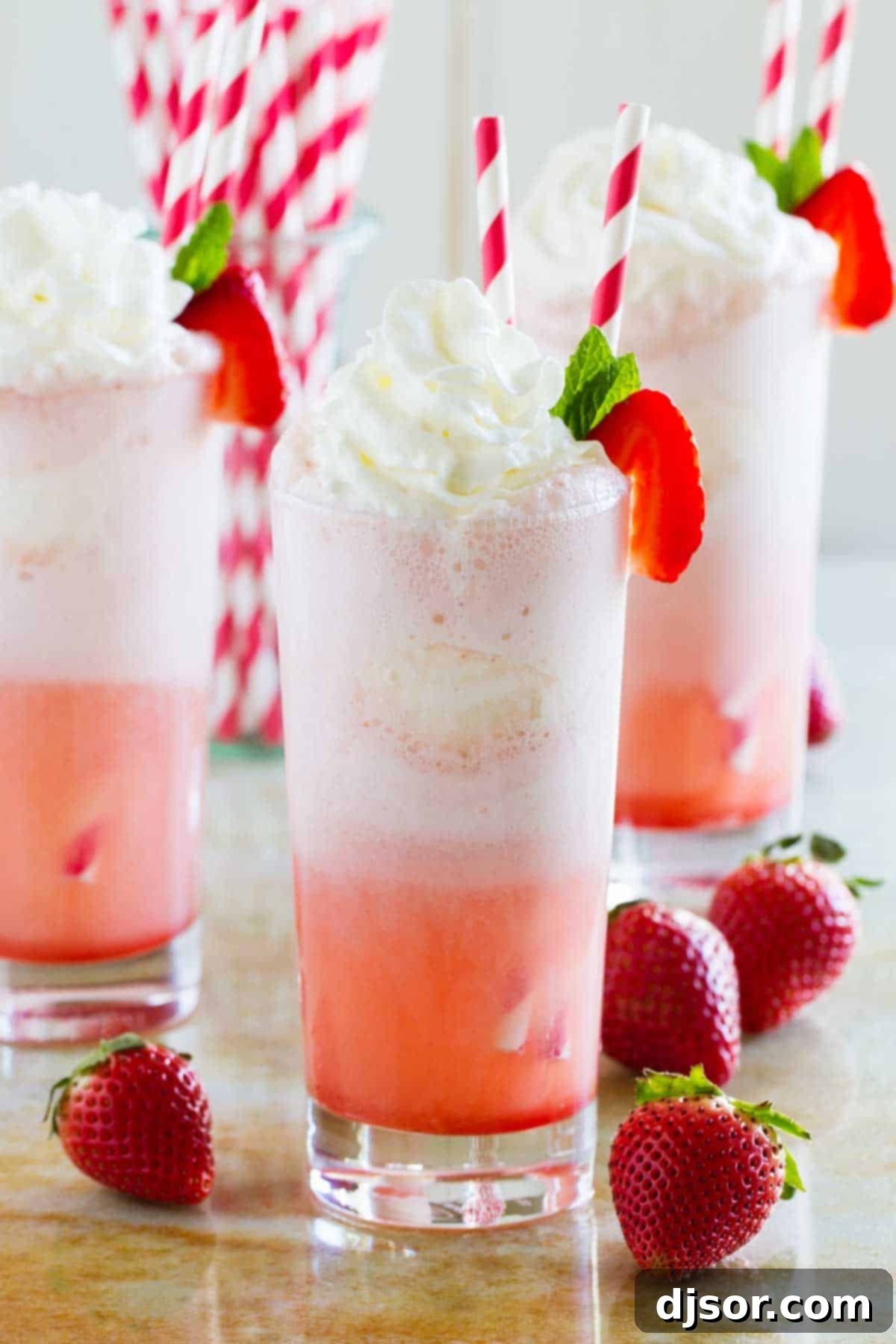 Three vibrant Strawberry Cream Floats, each topped with creamy whipped cream and a fresh strawberry garnish, sitting on a wooden surface.